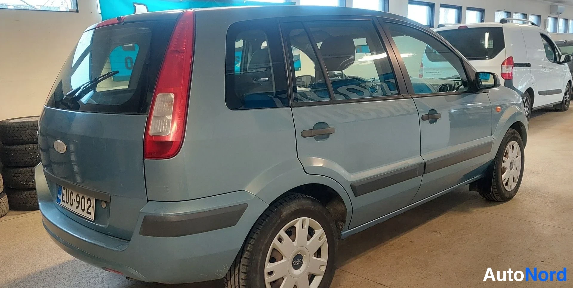 Takaviisto: Ford Fusion -farmariauto takaviistosta oikealta, vaaleansininen korivalmiissa tilassa sisätiloissa, rekisterikilpi.