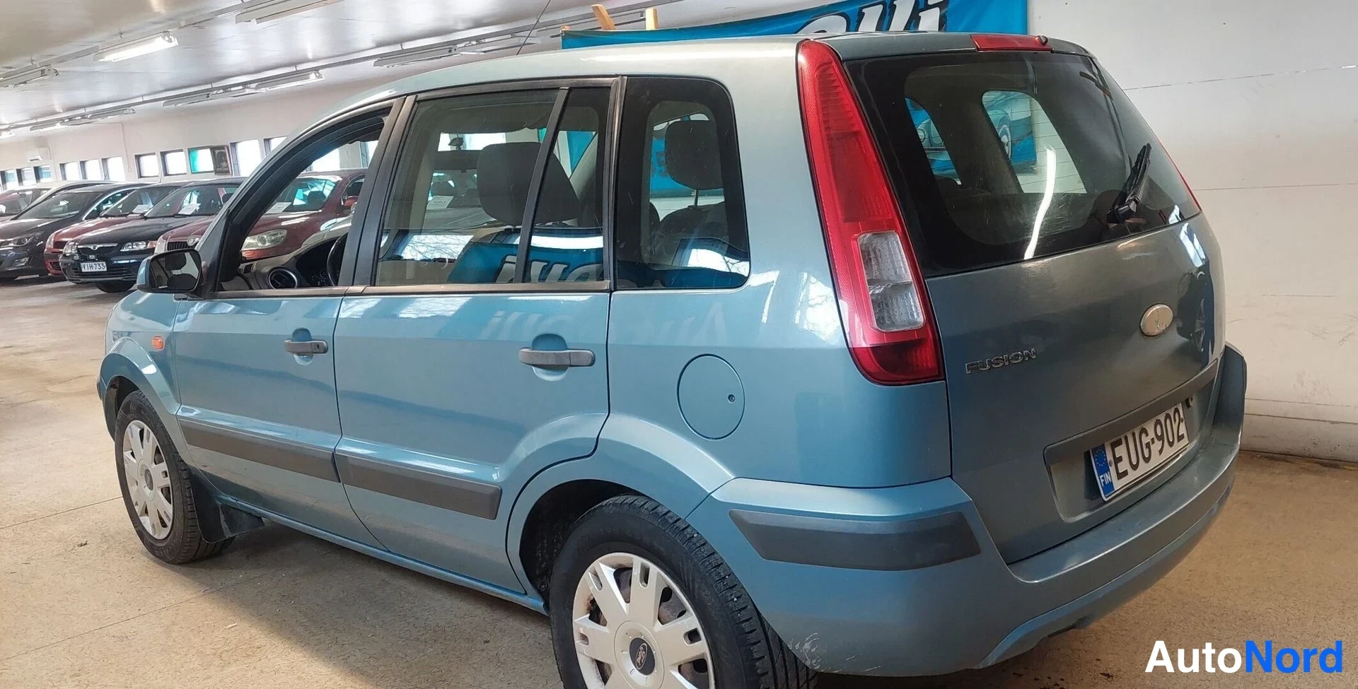 Takaviisto: Ford Fusion -farmariauto takaviistosta vasemmalta, vaaleansininen korivalmiissa tilassa sisätiloissa, rekisterikilpi.