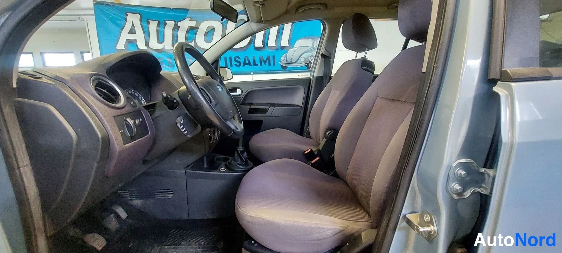 Muu: Ohjaamo vasemmalta: ohjauspyörä, mittaristo, manuaalivaihde ja kaksi etupenkkiä tummilla penkeillä.