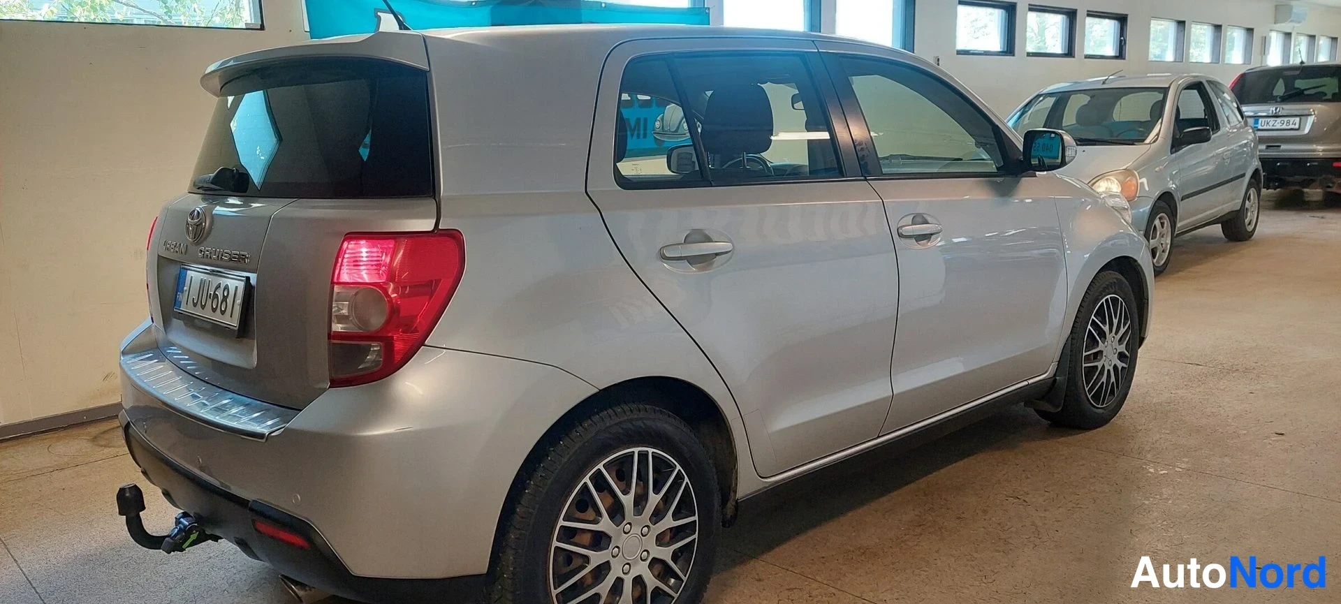 Takaviisto: Hopeanharmaa Toyota Urban Cruiser takakulmasta vasemmalta kuvattuna; takavalot, peräluukku ja J UJ-681-rekisterikilpi näkyvät, takavarrassa vetokoukku.