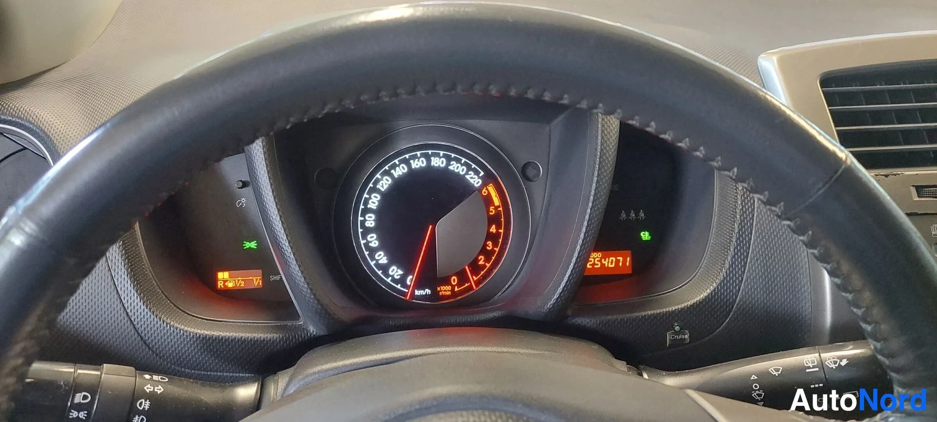 Edestä: Kojelaudan mittaristo: nopeusmittari 0–220 km/h, matkamittari 254071, varoitussymbolit syttyneinä.
