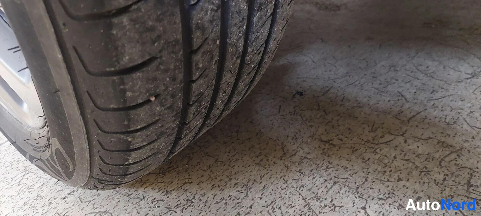 Muu: Lähikuva auton kesärenkaan kulutuspinnasta sementtilattialla.