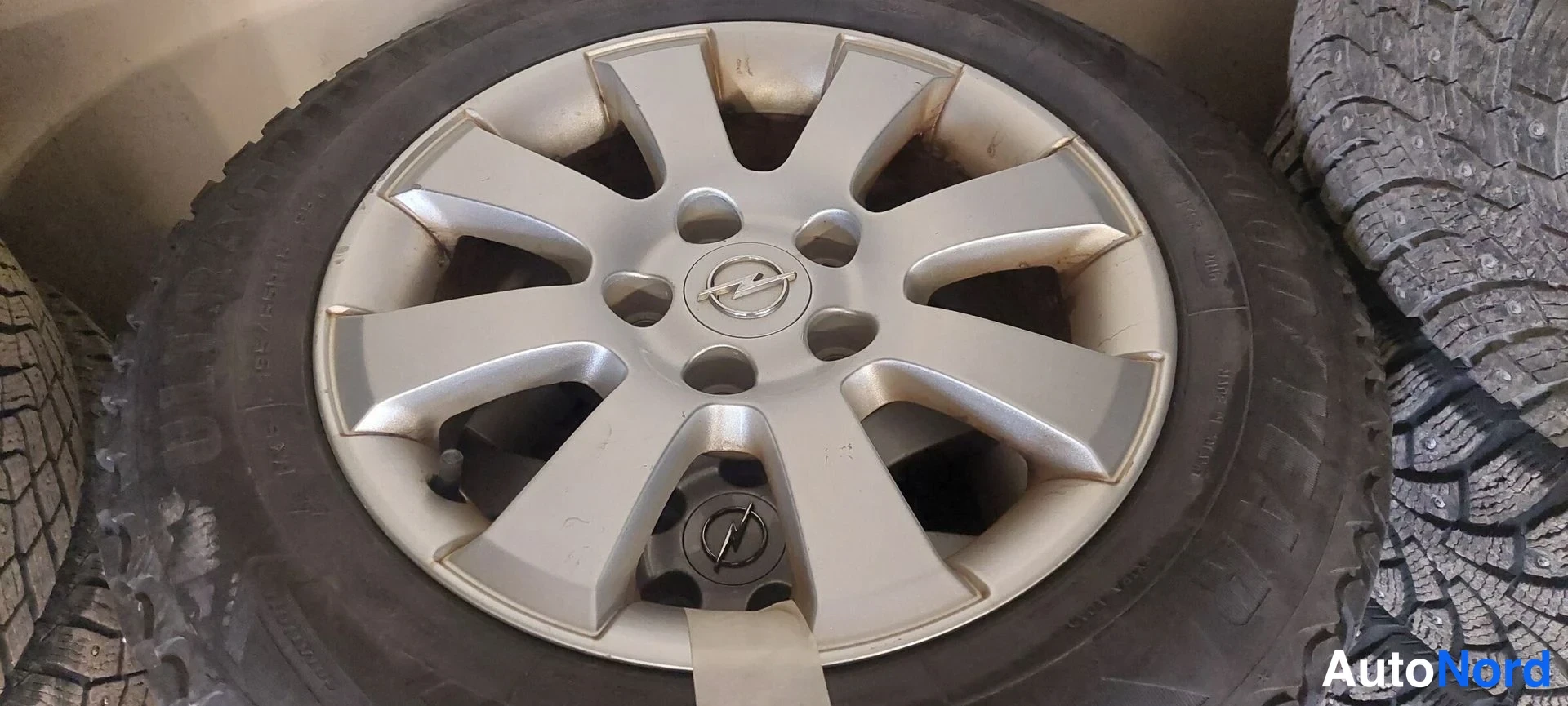 Muu: Opel-merkkinen hopeanvärinen alumiinvanne mustalla renkaalla varustettuna, muiden renkaiden ympäröimänä.