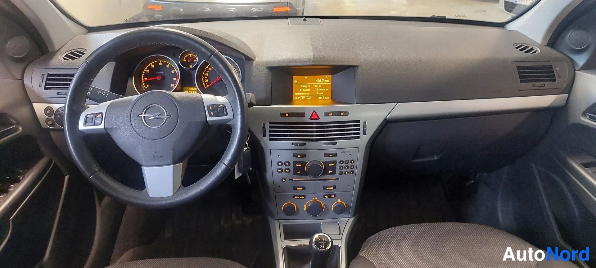 Muu: Ohjaamo näkyy etualalla Opel-merkkinen ohjauspyörä ja mittaristo, keskikonsolissa näyttö ja radiopaneeli.