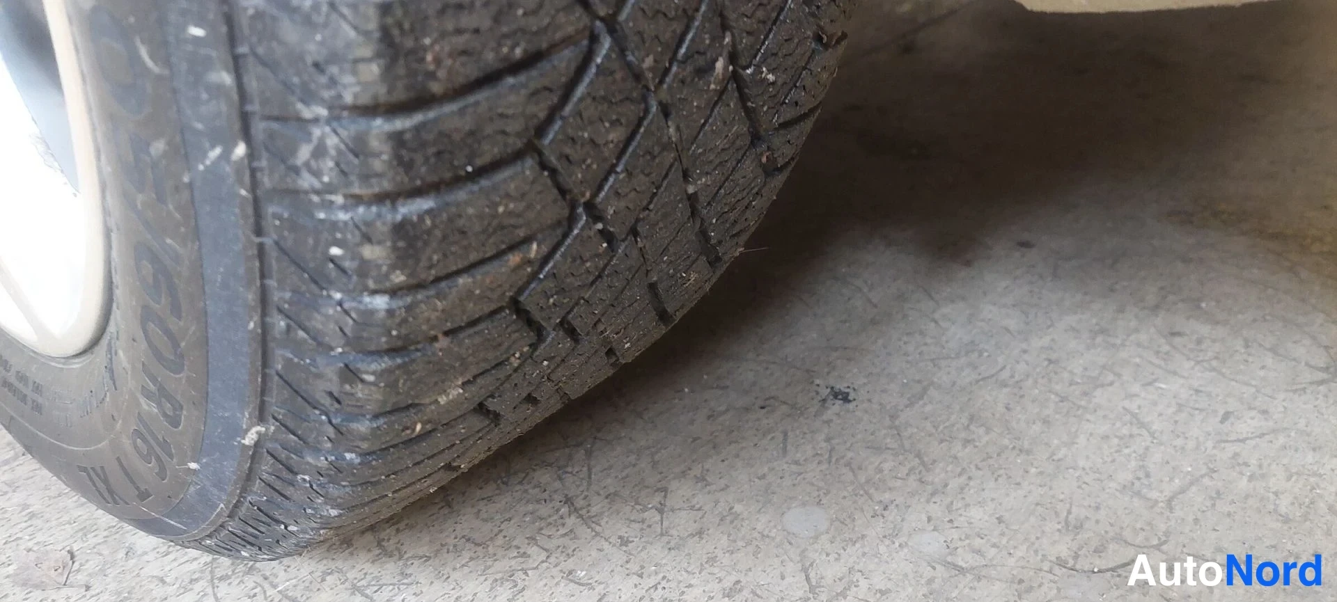 Yksityiskohta: Lähikuva auton takarenkaan pintakuviosta; renkaassa lukee osittain 195/60R16, auto seisoo betonilattiassa.