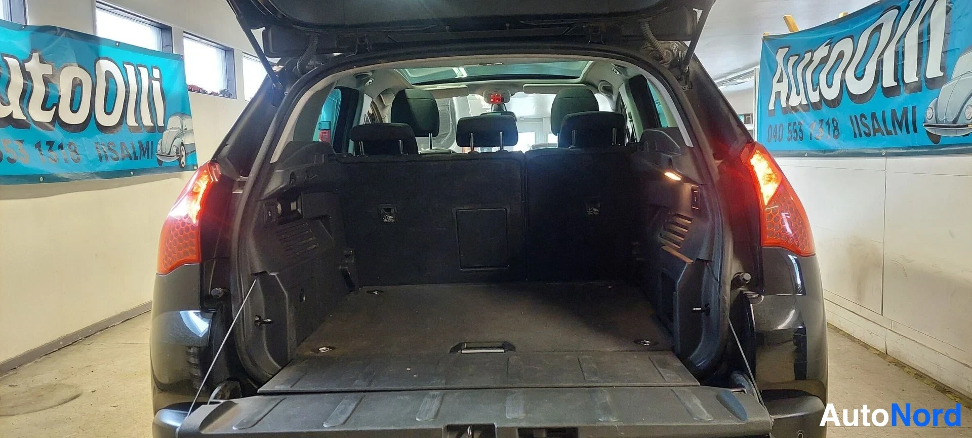 Takaa: Tavaratila taakse avattu: nousevat takapenkut ja pehmeä musta hylly, AutoOlli-mainokset taustalla.