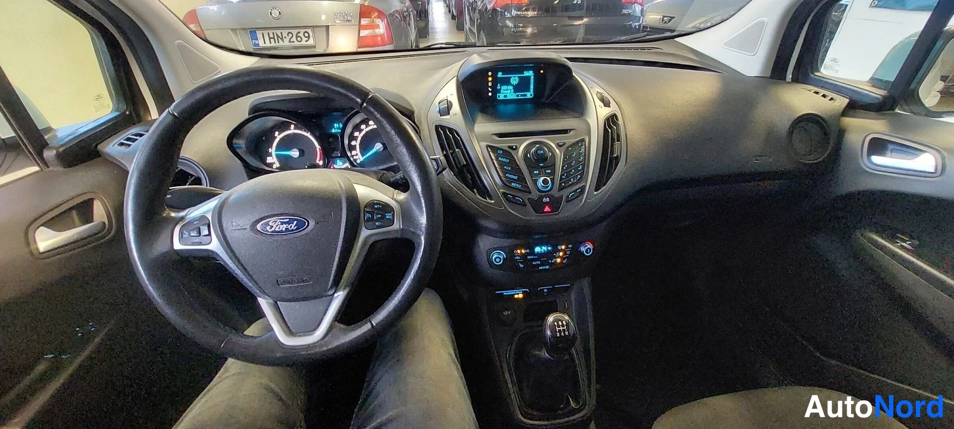 Yksityiskohta: Fordin ohjaamo etuosasta: ratissa Ford-merkki, digitaaliset mittarit, kosketusnäyttö ja radio, manuaali vaihdekepilla; istuin kuljettajan puolella.