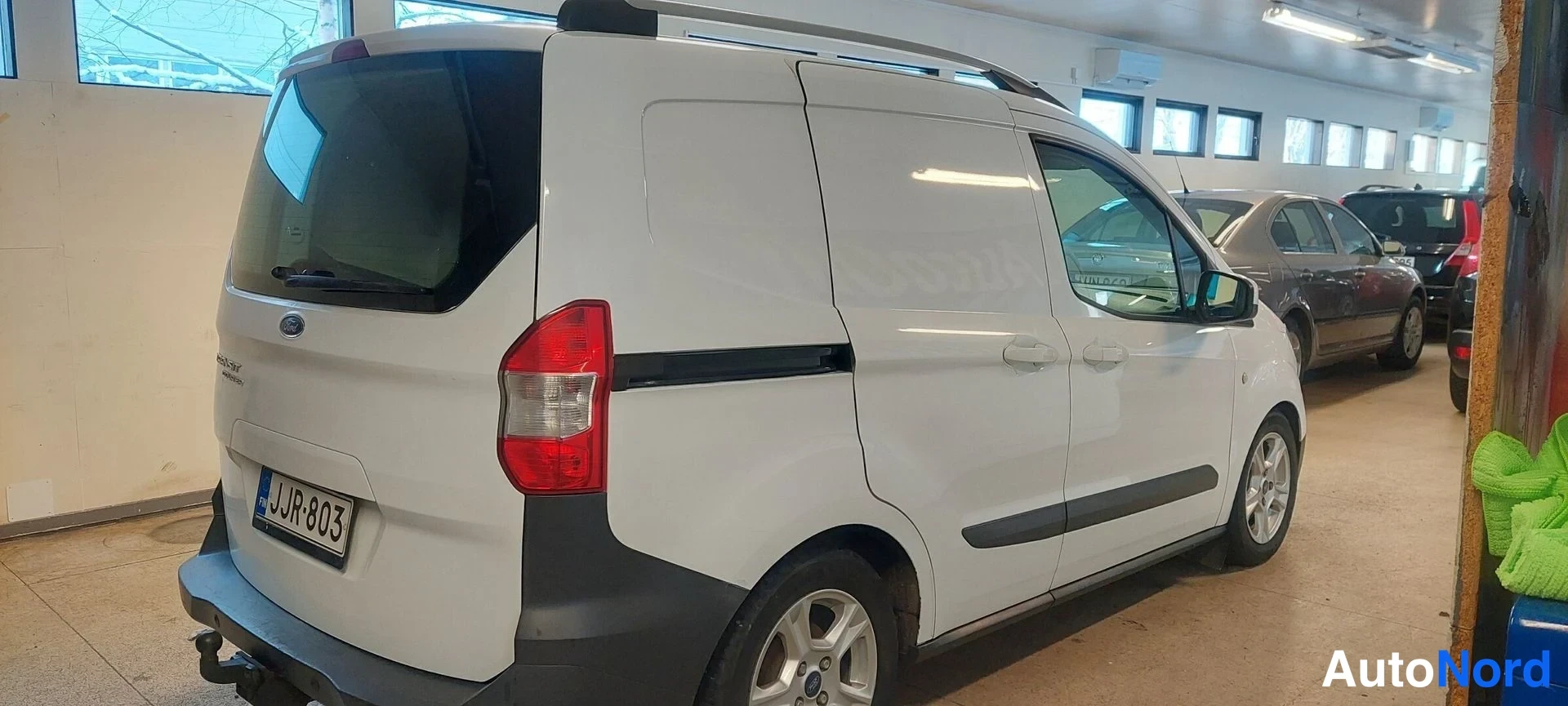 Takaviisto: Valkoinen pakettiauto takaosasta vasemmalta, perä ja kylki näkyvät hallissa.