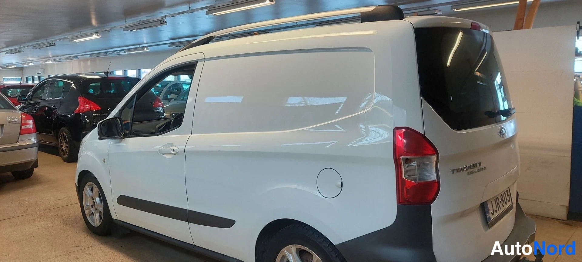 Takaviisto: Valkoinen pakettiauto takaosasta oikealta, perä ja kylki näkyvät hallissa.