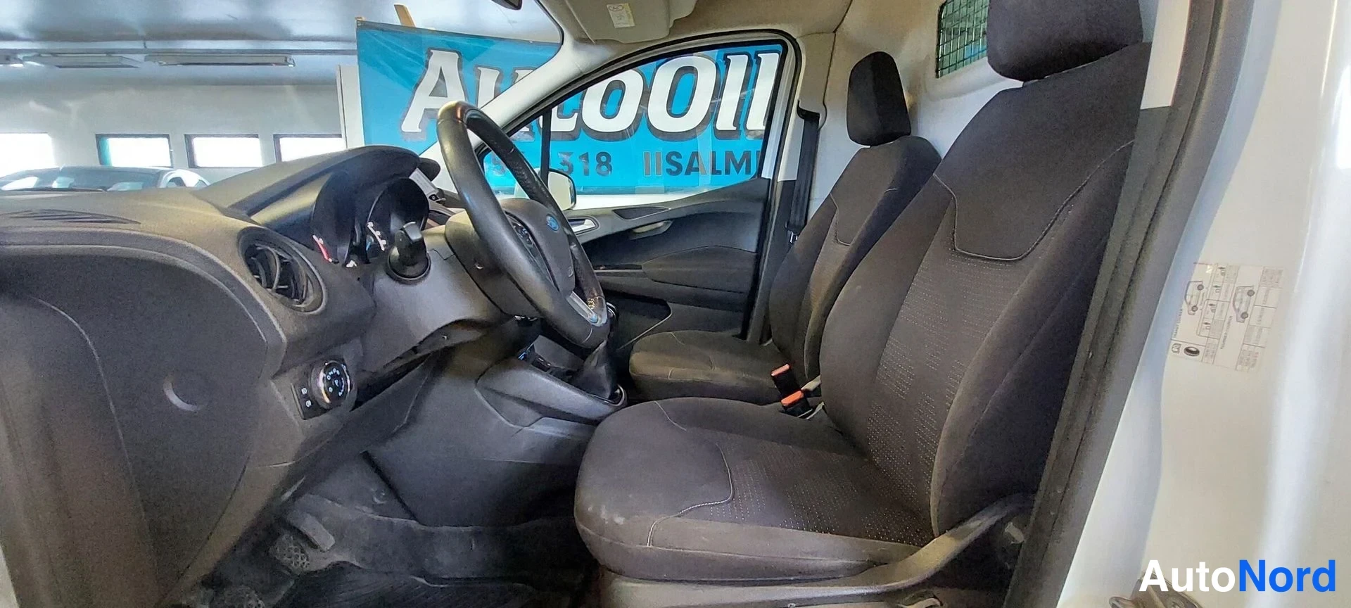 Muu: Kuljettajan ja etumatkustajan istuimet sekä kojelauta ja ohjauspyörä Ford Transit Courierin sisällä.