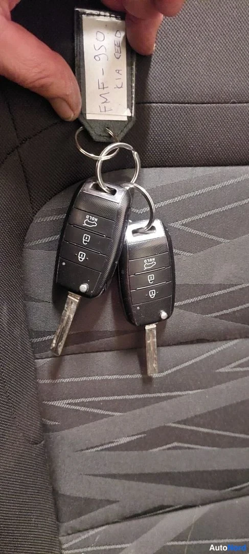 Muu: Kaksi Kia-avainketjua ja käsin kirjoitettu lapseton lappu tekstillä ' KIA CEED' tummaa kankaanpäällistä istuinta vasten.
