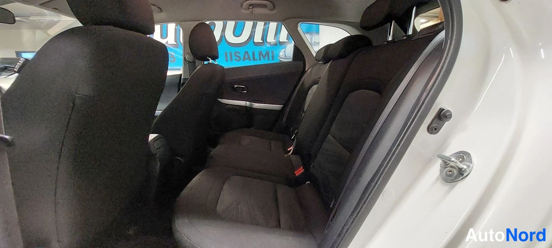Muu: Kia Ceed Farmari takaistuin.mustaa kangastakapenkkiä ja luuta; kaksi erillistä istuinta näkyvät; auton runko näkyy valkoisena ovenkarmiin.