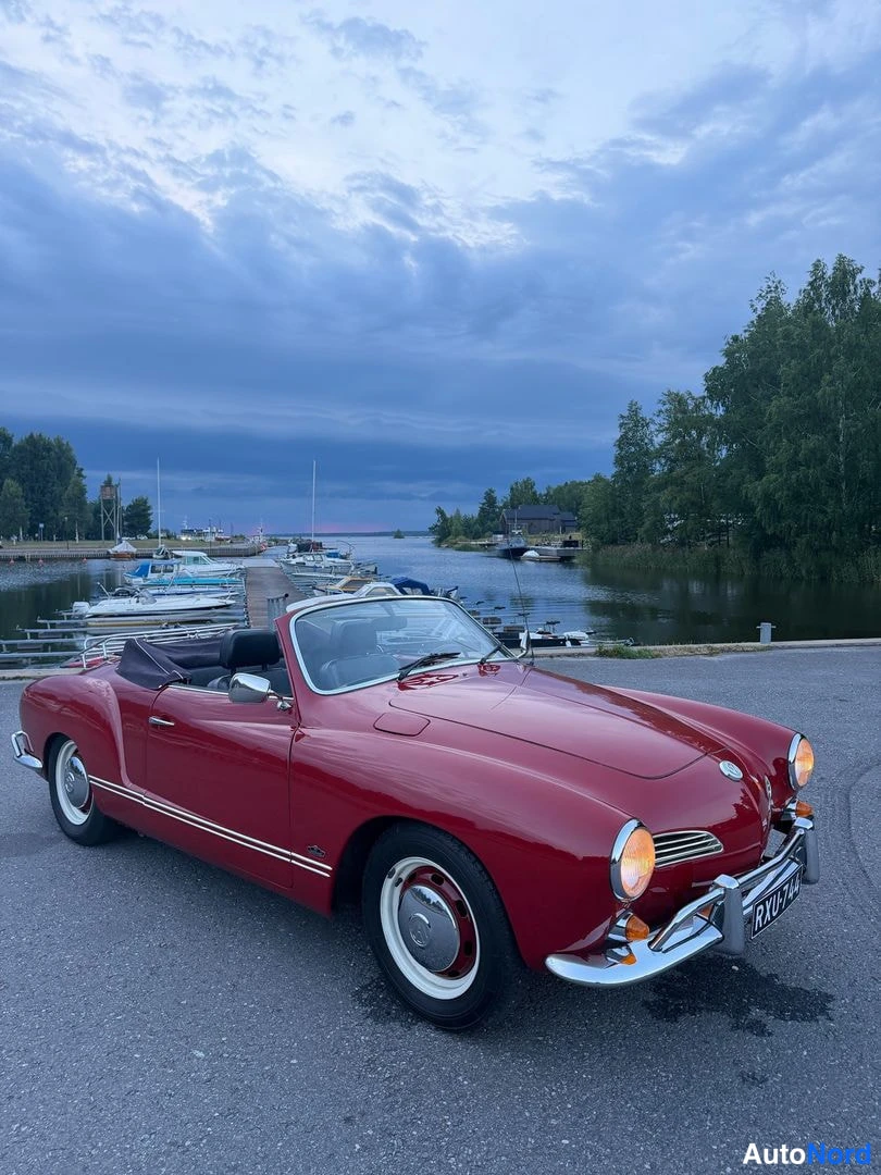 Etuviisto, nokka oikealle: Punainen avokauto etuviistosta oikealta satamassa, avattu kangaskatto taitettuna, valkoreunaiset pyörät.