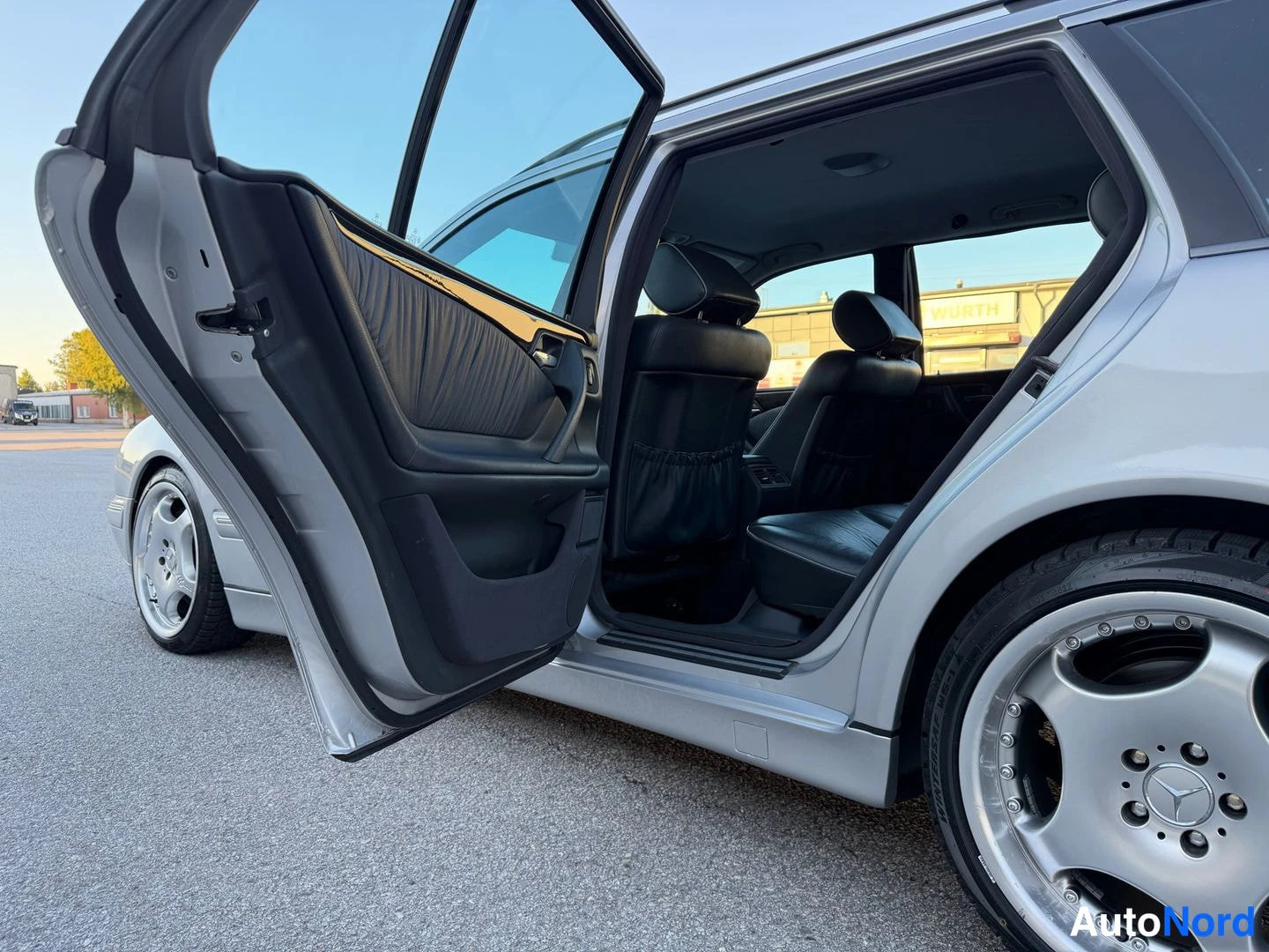 Muu: Hopeisen farmariauton etuovi auki, näkyvissä musta ovin paneeli, takaistuin ja Mercedes-merkintäinen kevytmetallivanne.