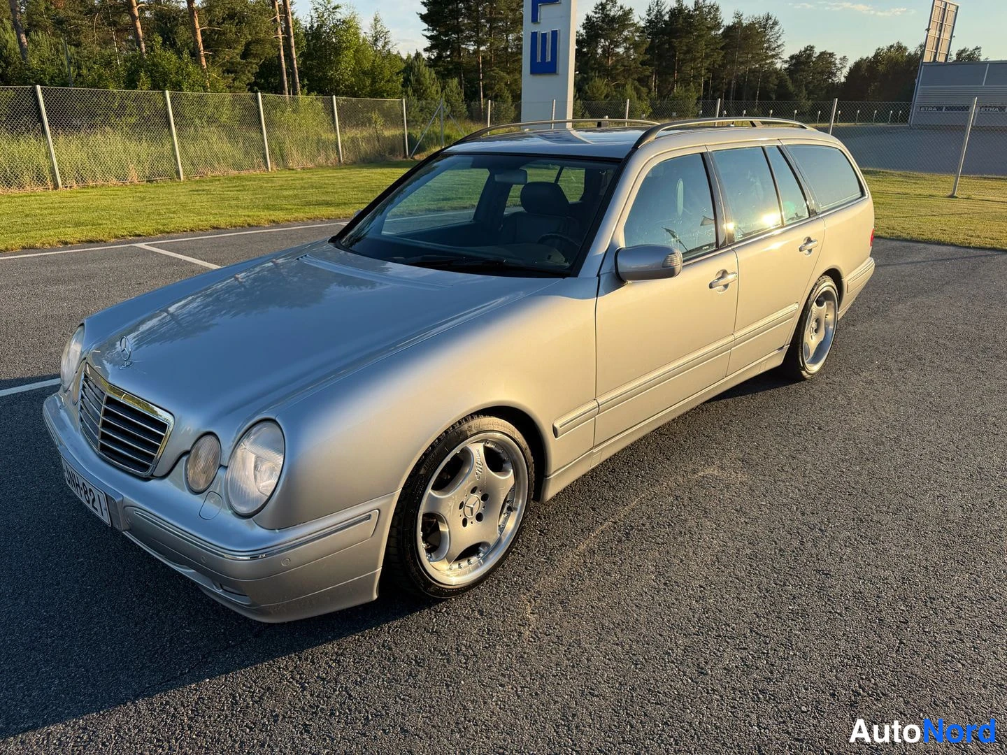 Etuviisto, nokka vasemmalle: Hopeanvärinen Mercedes-Benz farmariauto kolmivartalokulmassa vasemmalta edestä kuvattuna, etusäleikkö ja rekisterikilpi näkyvissä.