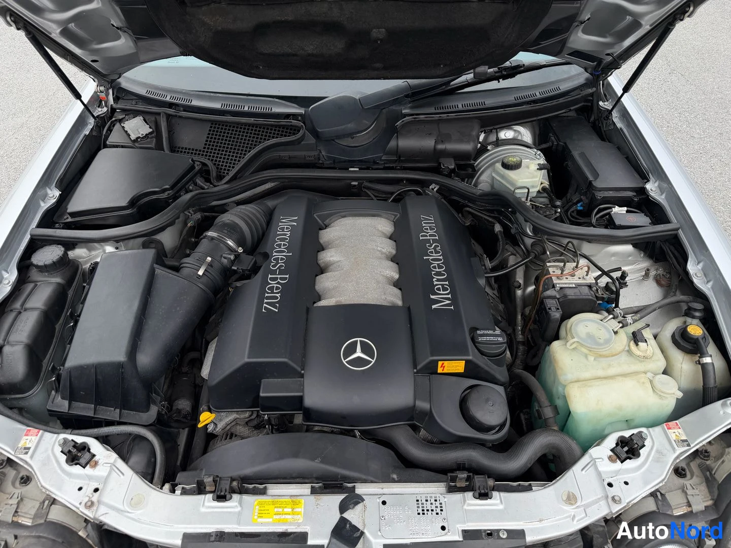 Muu: Moottoritila avattuna: musta moottorin suojakansi, jossa Mercedes-Benz-teksti ja tähti, ilmaussuodatinlaatikko vasemmalla ja jäähdytinnesteainelokko oikealla.
