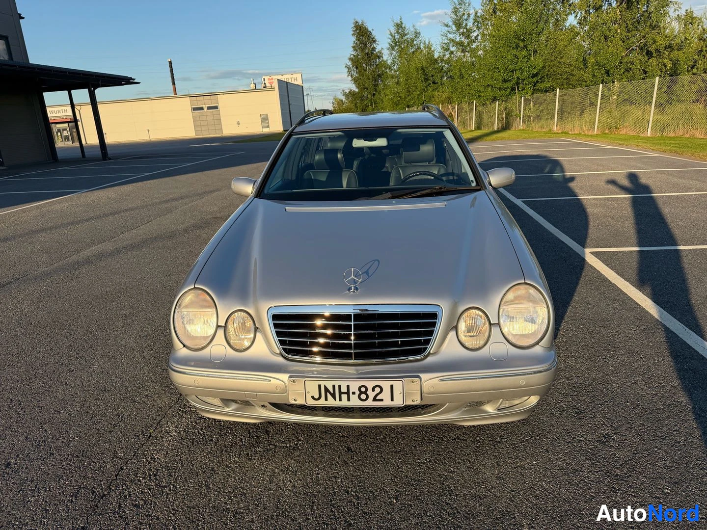 Edestä: Hopeisen farmariauton etupää suoraan edestä; rekisterikilpi ja Mercedes-tähti konepellillä