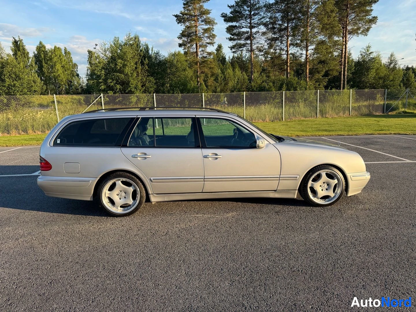 Sivulta: Hopeanvärinen farmariauto sivulta vasemmasta sivusta, auringonvalossa parkkipaikalla.