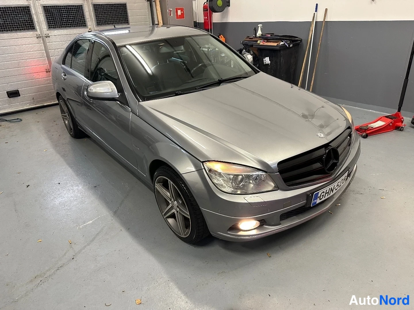 Etuviisto, nokka oikealle: Hopeavalkoinen Mercedes-Benz C-sarjan sedan etukulmasta vasemmalle kuvattuna autotallissa.