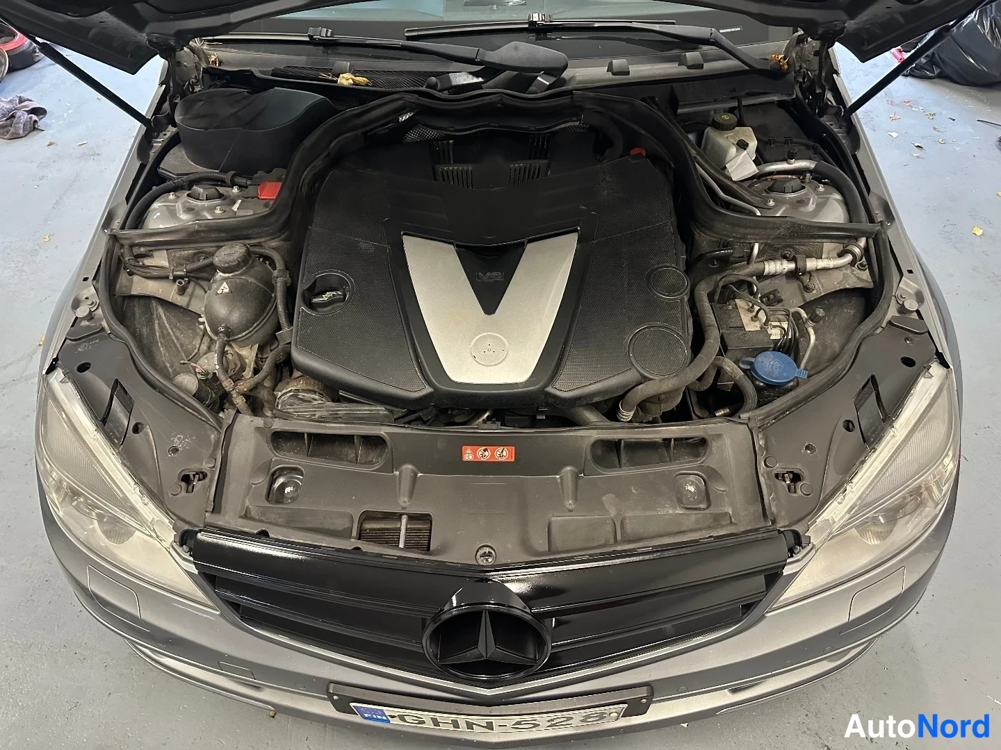 Edestä: Moottoritila kuvattuna ylhäältä, Mercedes-V6-merkitty moottorin kansi ja musta maski, konepelti auki