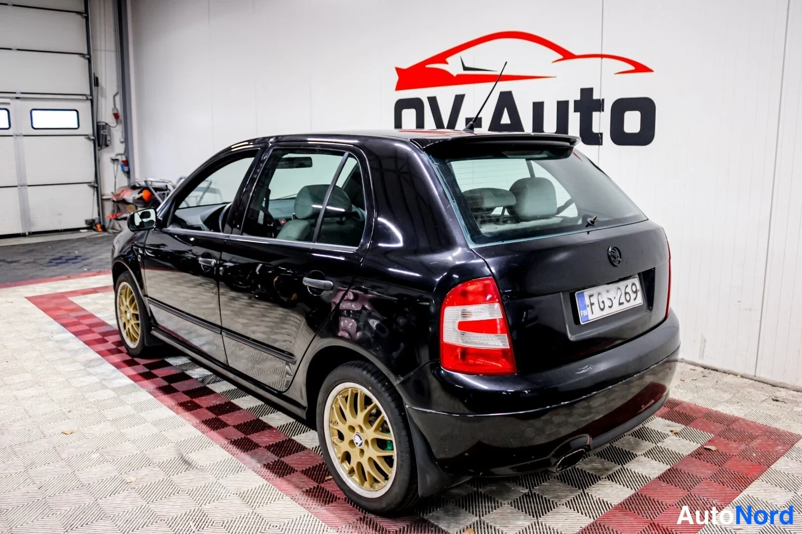 Takaviisto: Mustan hatchbackin takakulma sisätiloissa, keltainen vanteen väri takarenkaassa ja rekisterikilpi näkyvät.