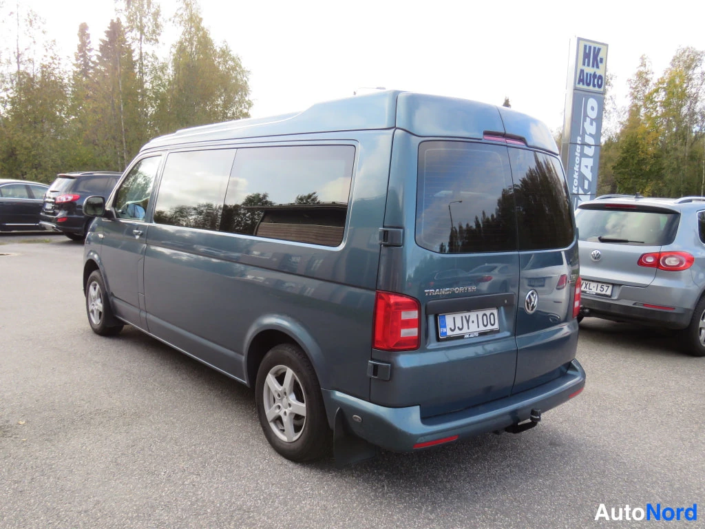 Takaviisto: Sinertävänharmaan Volkswagen Transporter -pakettiauton takakulma ja sivu parkkipaikalla, perä ja kylki näkyvät.