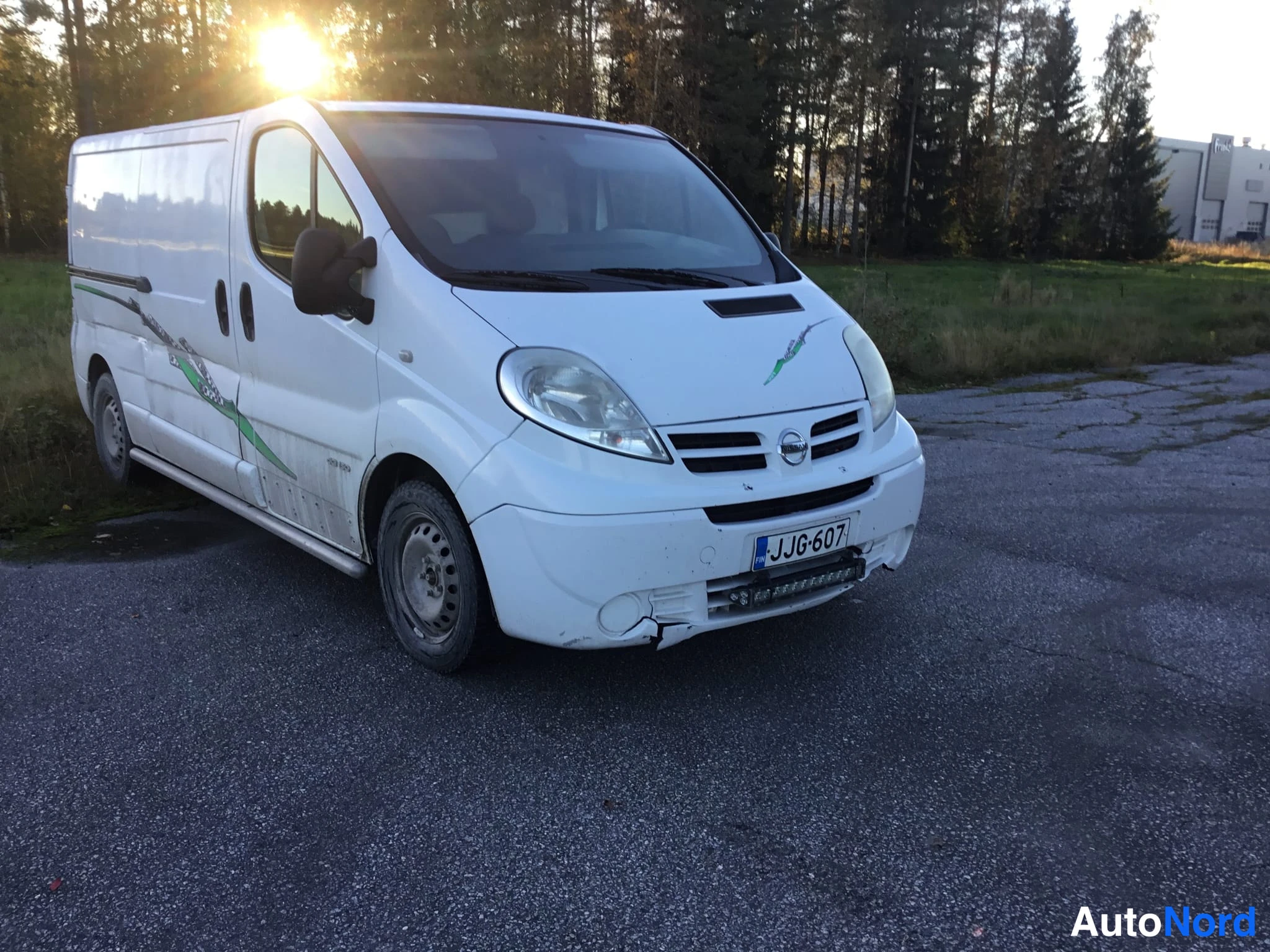Etuviisto, nokka oikealle: Valkoinen pakettiauto kolmeneljännes-kulmassa nokka oikealla, rekisteritunnus näkyvissä.