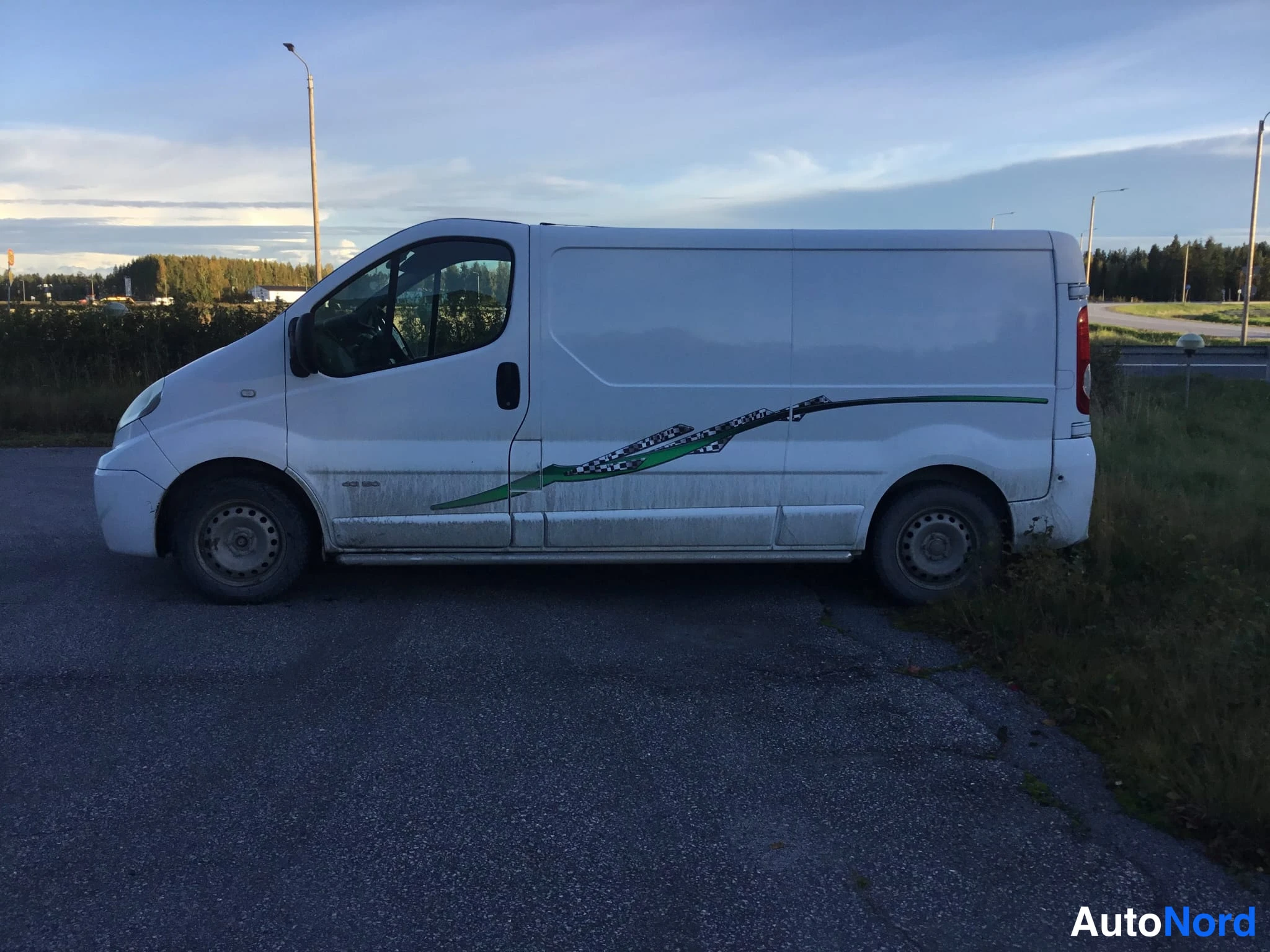 Sivulta: Valkoinen pakettiauto sivulta, vihreä koristekuviointi ovissa.