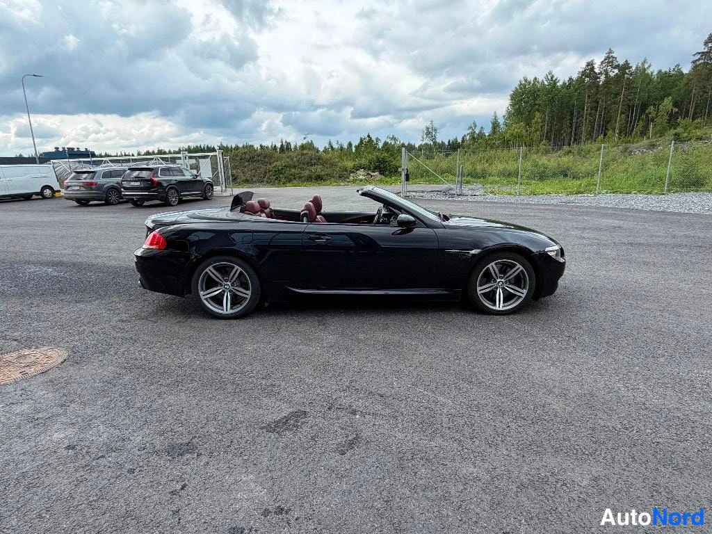 Takaviisto: Musta avomallinen urheiluauto kolmasosan takanäkymässä, sivuprofiili näkyvissä, parkkihallilla.