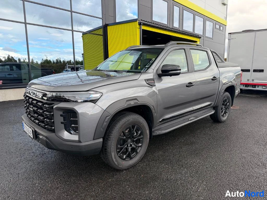 Etuviisto, nokka vasemmalle: harmaa Maxus T60 -naksi etukulmasta talon edessä, mustat vanteet.
