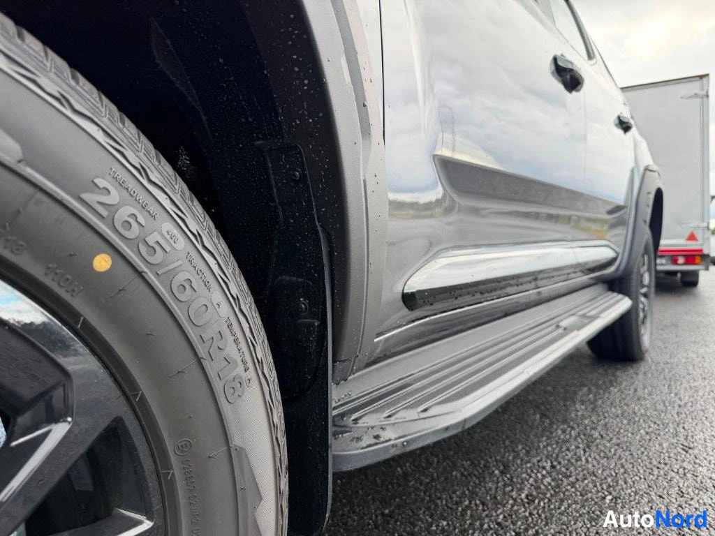 Sivulta: Sivunäkymä autosta matalasta kulmasta: rengas, musta lokasuojaliuska ja metallinen sivukaide, kori harmaa.