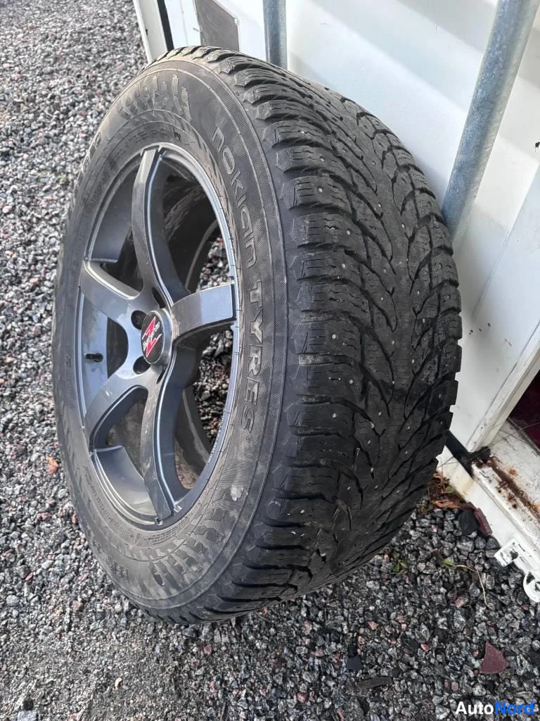 Yksityiskohta: Irrotettu rengas alumiinivanteella seisoo sorapinnalla; renkaan sivuseinässä lukee 'Nokian Tyres'.