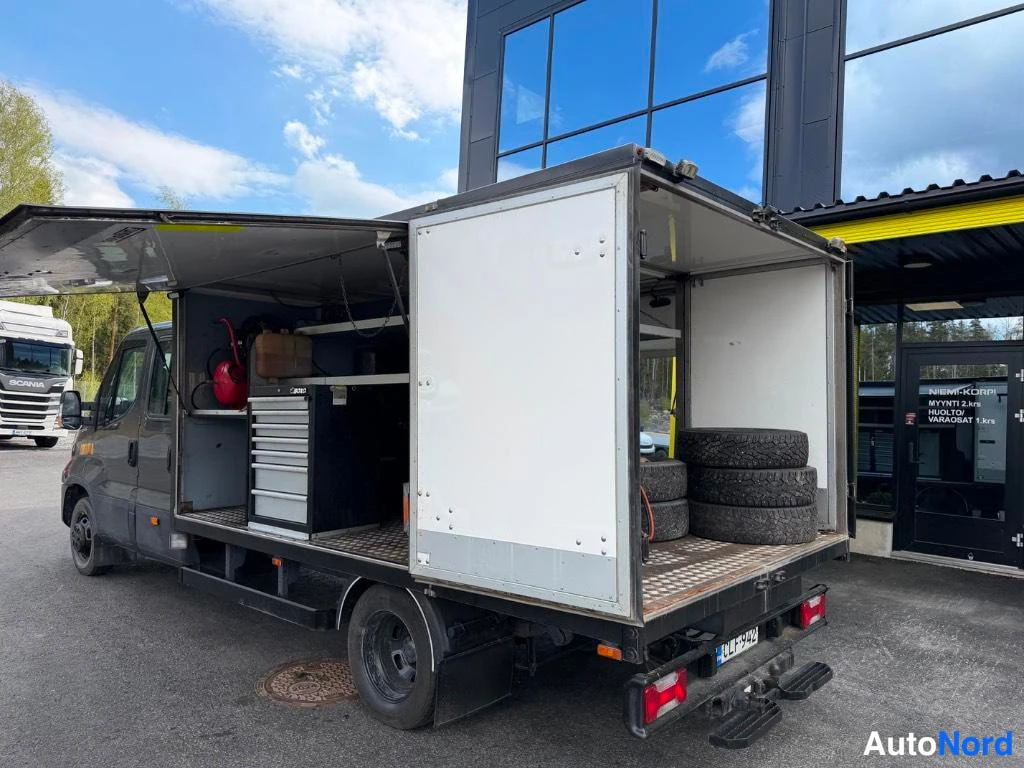 Sivulta: Side view of the grey Iveco Daily maintenance truck with side door open revealing interior tools and storage compartments.