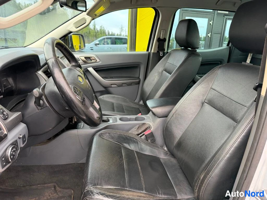 Ohjaamo: Interior shot from passenger side looking toward driver's seat, showing black leather front seats, steering wheel with Ford logo, dashboard controls, and yellow
