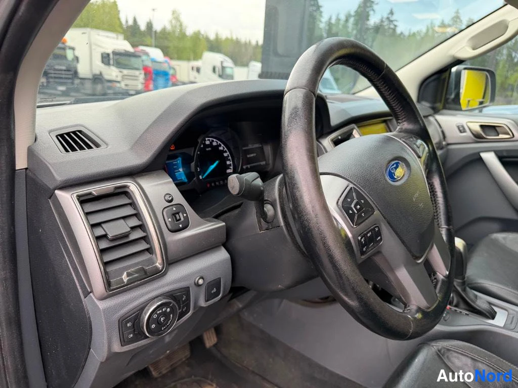 Etuistuimet: Driver perspective view showing black multi-function steering wheel with audio and cruise control buttons, instrument cluster with blue needles, air vent on lef