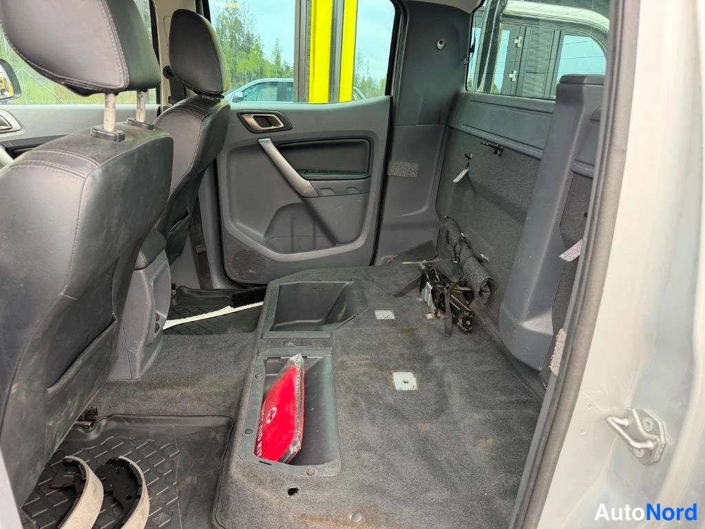 Takaistuimet: Rear cabin interior view showing black seats from behind, grey door panel with silver handle, floor area with storage compartments, and emergency warning triang
