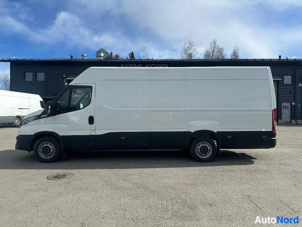 Etuviisto, nokka vasemmalle: Iveco-pakettiauto sivulta etuviistossa, valkoinen korimustat pyörät ja mustat puskurit, paikallaan piha-alueella.