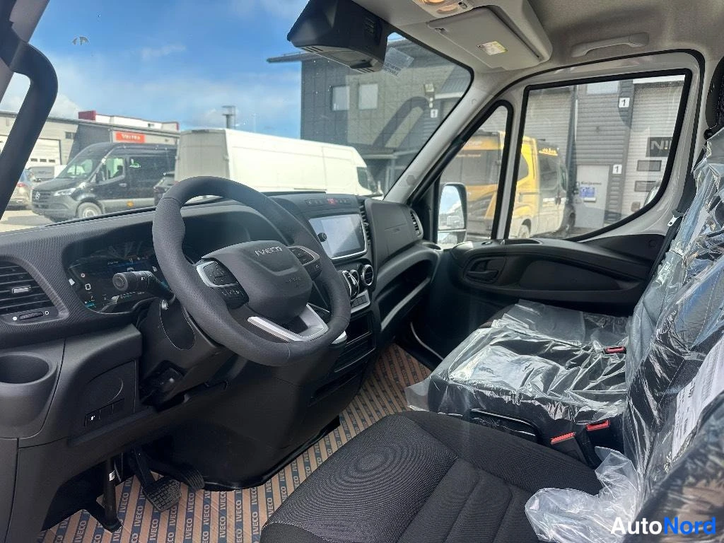 Edestä: Iveco-henkilönkuljetusautojen matkustamisen ohjaamo, musta ohjauspyörä, kojelauta ja infotainment-näyttö, istuimet suojamuovissa.