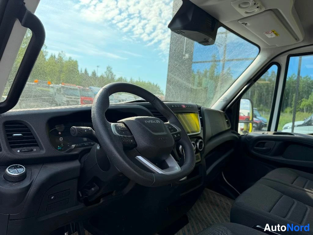 Muu: Iveco-hytin sisätilat ohjauspyörä ja kojelauta näkyvät, tuulilasin läpi kenttä muilla ajoneuvoilla.