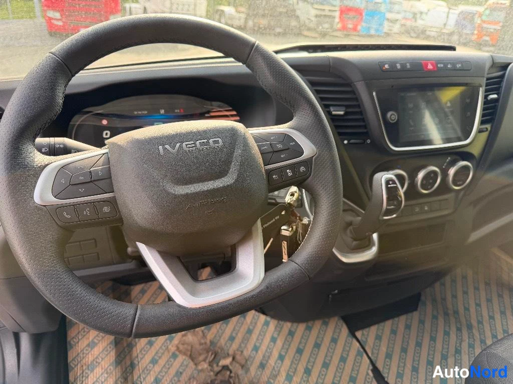 Muu: Ohjaamon sisäkuva: IVECO-logollinen ohjauspyörä, kojetaulun näyttö ja infotainment-näyttö, vaihteenvalitsin ja ripustetut avaimet.