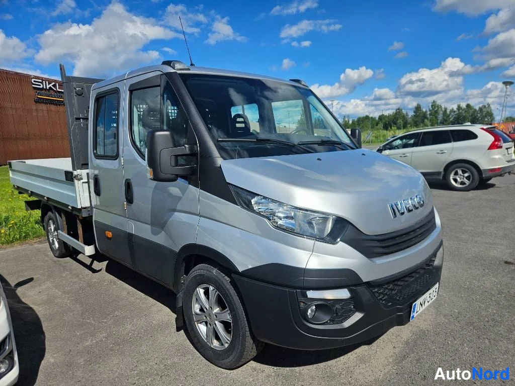 Etuviisto, nokka oikealle: Hopeanvärinen Iveco Daily lava-auto kolmannelta edestä oikealle, lavan sivupöytä ja nokka näkyvissä.