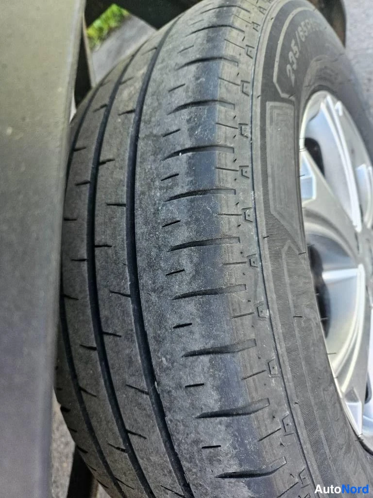 Yksityiskohta: Close-up of a dark grey rubber vehicle tire with visible tread pattern and an alloy wheel rim on the right.