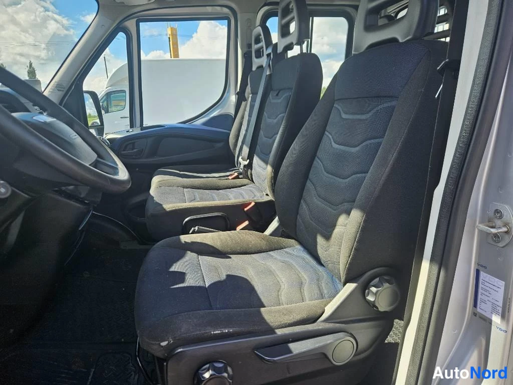 Etuistuimet: Side view from open driver door showing front cabin with black cloth two-bucket seats featuring side bolsters and manual adjustment knobs. A paper sticker is st
