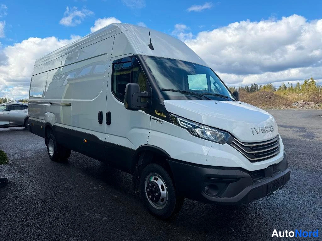 Etuviisto, nokka oikealle: Iveco Daily -pakettiauto edestä oikealta kolmanneskulmasta korkealla katolla parkkipaikalla.