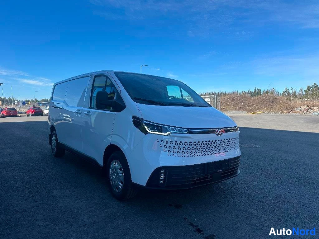 Etuviisto, nokka vasemmalle: Valkoinen Maxus-pakettiauto vasemmanpuoleisessa etuviistokuvassa aukiolla sinisen taivaan alla.