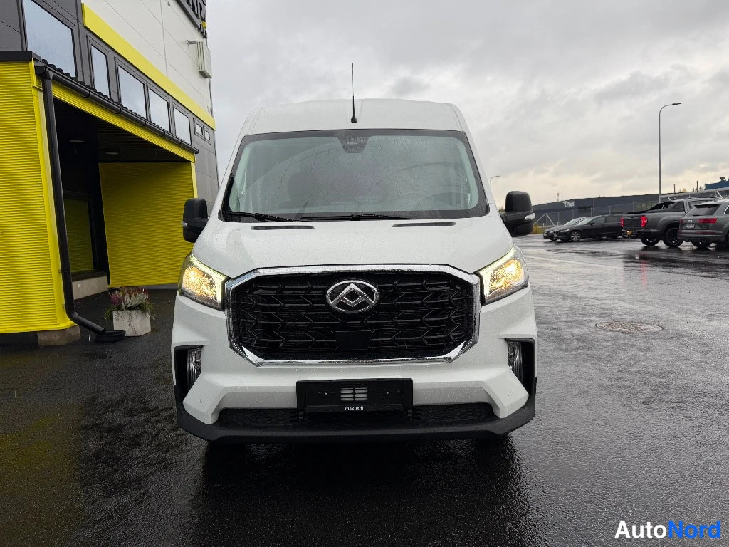 Edestä: Valkoinen Maxus Deliver 9 -pakettiauto suoraan edestäpäin, ajovalot päällä ja musta etusäleikkö.