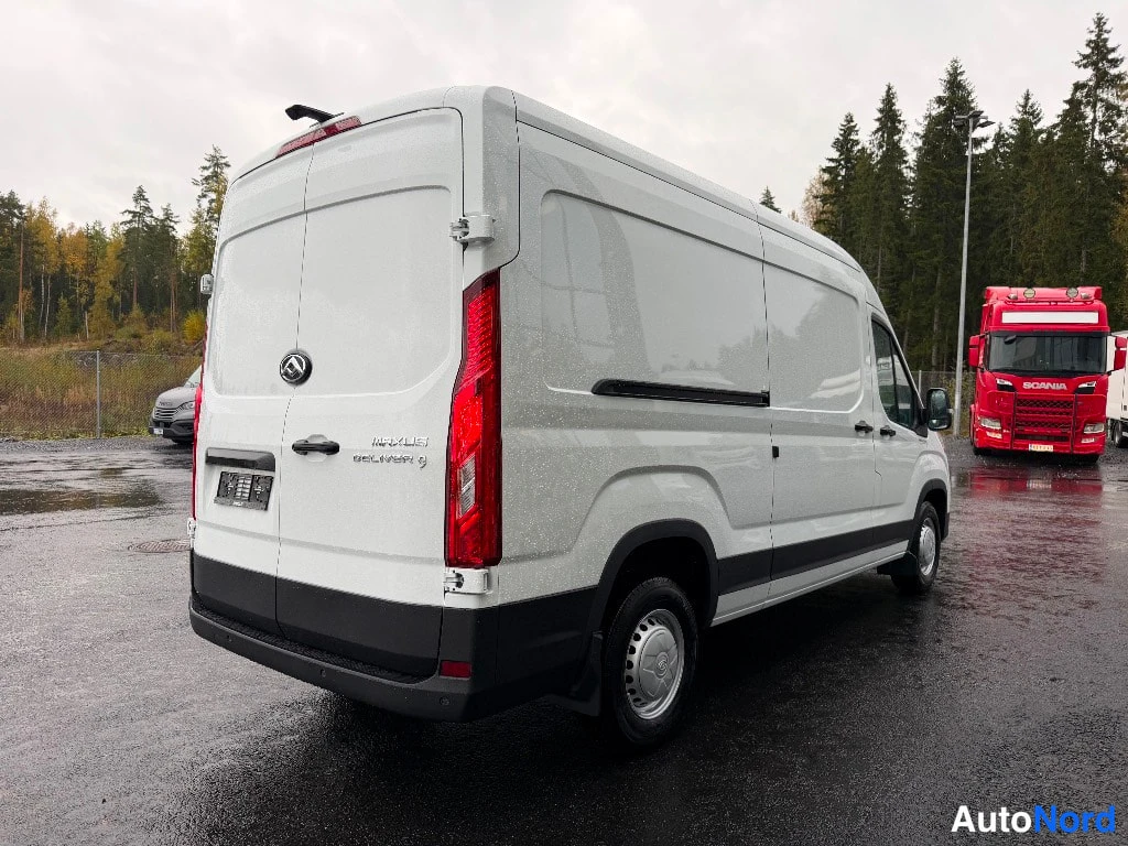 Takaviisto: Valkoinen Maxus Deliver 9 -pakettiauto takaviistosta, takavalot ja kaksois takaportit näkyvät, rekalla punainen Scania-kuorma-auto.