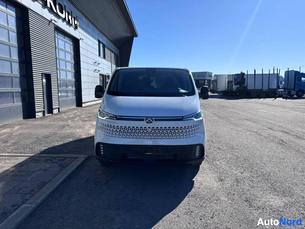 Edestä: Valkoinen Maxus Deliver 7 -pakettiauto suoraan edestä kuvattuna autotalon edessä.