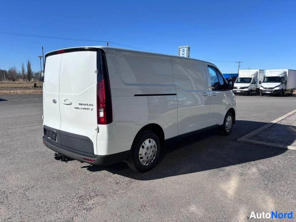Takaviisto: Valkoinen Maxus Deliver 7 -pakettiauto takaviistosta vasemmalle kuvattuna parkkialueella.