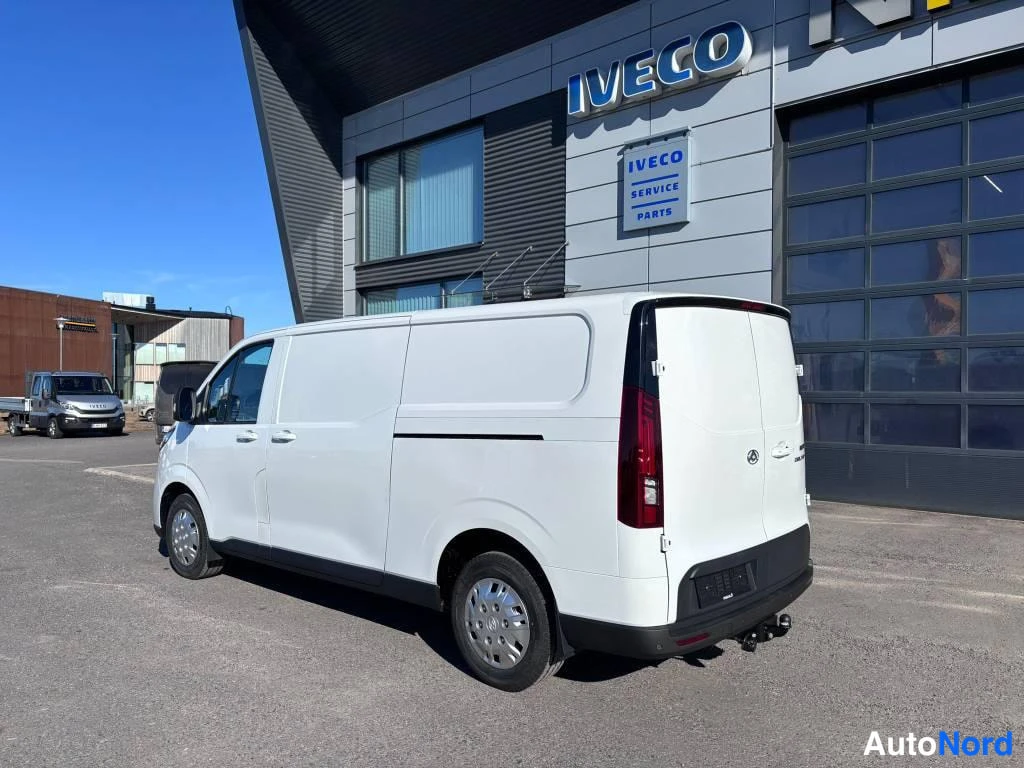 Takaviisto: Valkoinen pakettiauto kolmannes­kulmassa takaa oikealta sivulta, takaovi ja kyljy näkyvissä IVECO-hallikia rakennuksen edustalla.
